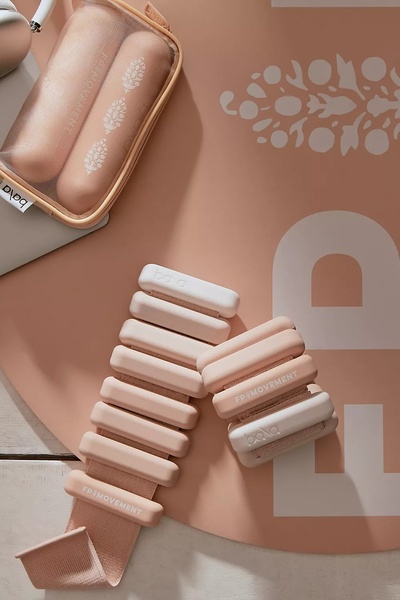 A top-down, clean product shot of tonal wearable weights and their carrying case on a soft-toned yoga mat.